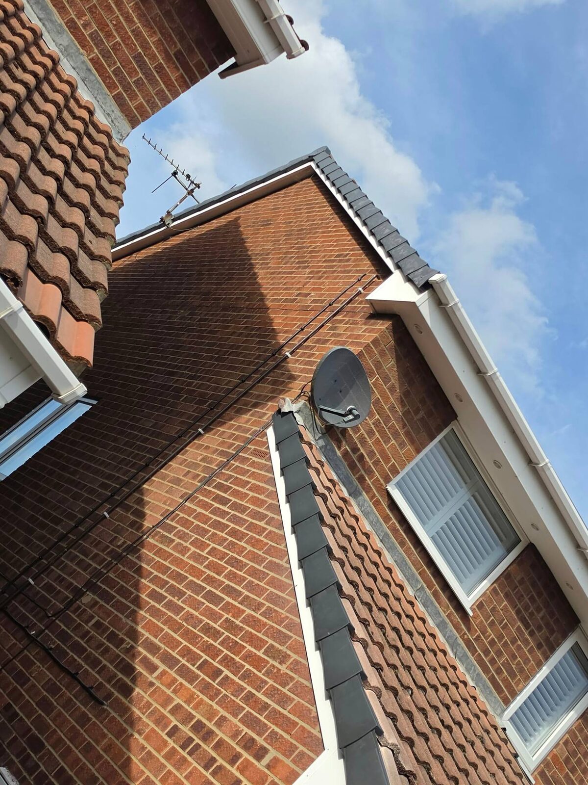 Looking up at new grey dry verge caps along the gable edge of a brick house with white fascia and soffit