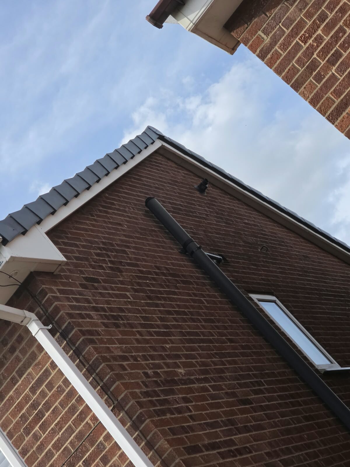 Full gable end of a brick house finished with grey dry verge caps and white fascia boards